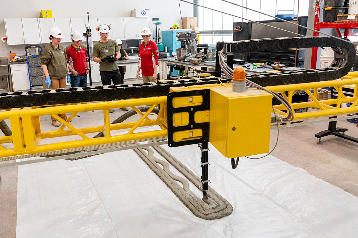 University of Arkansas faculty and students work together in a lab with a 3d cement printer